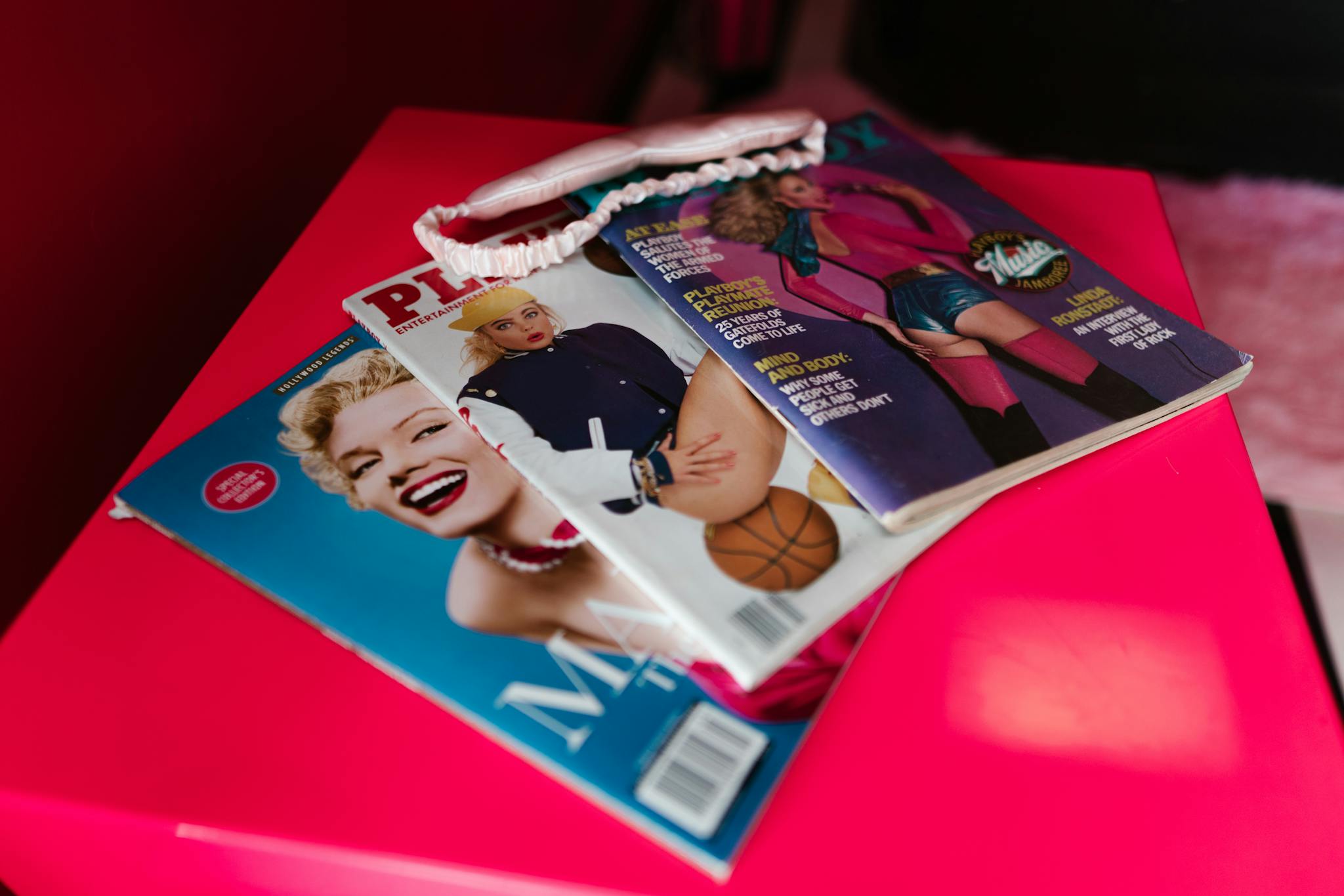 A close-up view of fashion magazines on a pink surface, featuring vibrant covers and a headband.